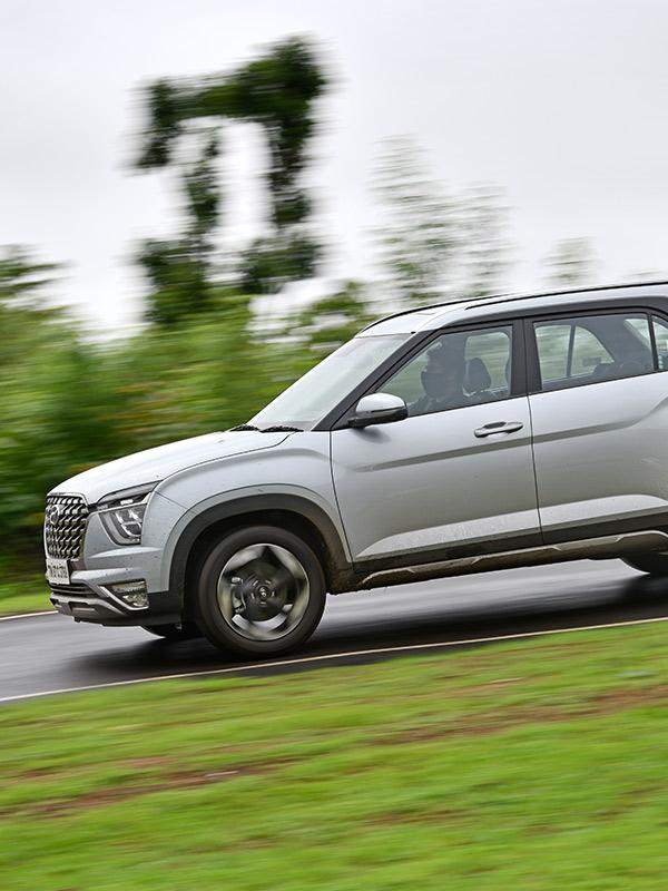 Vista lateral de Hyundai Creta Grand color plata descendiendo un camino mojado en pendiente